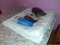 Overall lot on mattress: white eyelet comforter folded with packaged duvet covers and burgundy fleece blanket on top