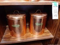 Two large copper biscuit canisters on shelf