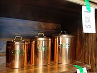 Front view of three copper canisters showing size variance and label plates