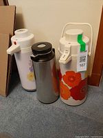 Three airpot thermoses standing together showing designs and condition