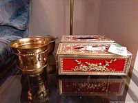 Brass planter and ornate red tissue box cover on glass table