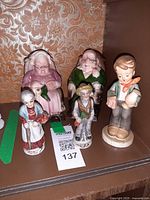 Five ceramic figurines including pair of seated coin banks and three standing figures