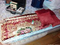 Bedspread folded with two pillows on top, case of unrelated items in background