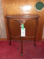 Front view of wooden demi-lune table showing curved front, cabriole front leg, stretcher