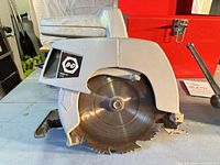 Left side view of Black & Decker 7301 circular saw showing blade guard, B&D logo, and red toolbox partially visible