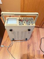 Front view showing CRT, controls, carry handle, attached power cord