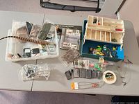 Overview of lot on table: tackle box, lures, fly-tying materials, books, weights