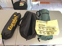 Overview of Eureka Solitaire tent bag, black accessory bag, rolled green sleeping pad with instruction sheet