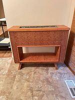 Front view of wood console cabinet showing textured front panel, open shelf, tapered legs