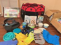 Group shot of all dog items including assembled playpen, sling, bowls, harnesses, apparel, books, bark collar
