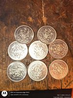 Eight Canadian 50-cent coins arranged on wooden surface, showing Coat of Arms side