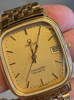 Close view of dial showing Omega logo, Seamaster Quartz text, gold-tone striped dial, baton markers, date window