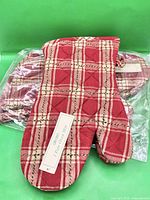 Pair of red plaid oven mitts sealed in plastic next to loose mitt