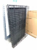 Folded black wire dog crate with tray leaning against wall