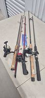 Four fishing rods with reels laid out side by side on surface