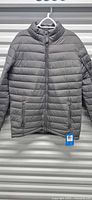 Front view of gray Columbia quilted jacket on hanger showing full-zip and pockets with tag attached