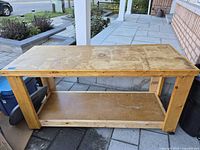 Full view of wooden workbench showing top, lower shelf, casters