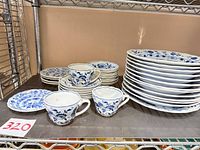Stacked dinner plates, side plates, bowls, cups, saucers on metal shelf