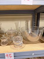 All items grouped on shelf: punch bowl, covered compote, bud vase, bell, lidded jar with spoon, cup and saucer