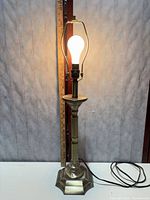 Full view of bronze-tone table lamp illuminated, ruler for scale