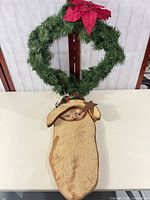 Wreath and wooden Santa plaque shown together on table
