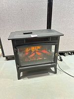 Front view of Duraflame electric stove heater with remote on top and power cord visible