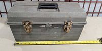 Closed grey plastic toolbox with measuring tape showing length and rusted latches