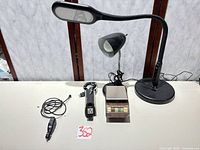 All items arranged on table: two desk lamps, car inverter, cord, scale