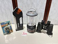 All four items side by side: packaged headlamp, work light, lantern, binoculars
