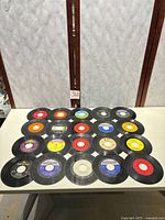 Top-down view of roughly twenty 7-inch singles arranged in four rows, showing assorted label colours and centre holes