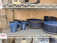 Three mugs, stack of dinner plates, stack of salad plates on wire shelf