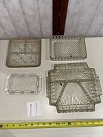 Overview of four clear Depression glass divided trays next to tape measure
