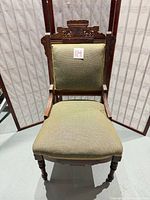 Front view of carved wood chair with olive upholstery