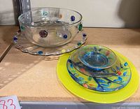 Large clear glass bowl with coloured dots on matching underplate beside lime-yellow plates