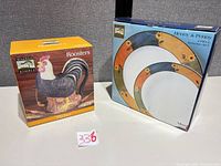Front view of both boxed items: Rooster pitcher and 2-piece serving set