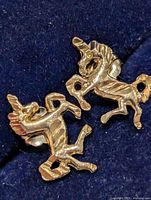 Front view of both gold unicorn earrings on dark background