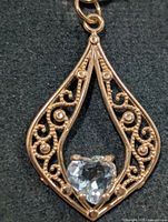 Front view of pendant showing filigree design and heart-cut blue topaz