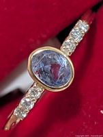 Close-up side angle of ring showing oval blue sapphire bezel set in yellow gold with diamond accents