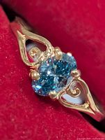 Front view of yellow gold ring with oval blue diamond and heart motifs