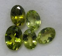 Five loose oval peridot gemstones on white background