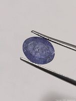 Oval violet-blue tanzanite held in tweezers