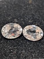 Two oval faceted clear stones on dark surface