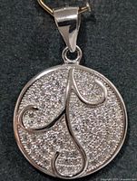 front view of round silver pendant with CZ stones and swirl