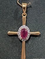 Front view of gold-tone sterling silver cross pendant with ruby and halo stones