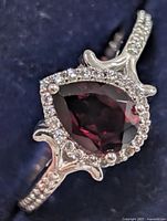 Front angled view of ring showing garnet, CZ halo, shoulder accents