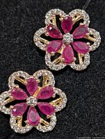 Close-up of floral silver earrings showing ruby petals and CZ halo