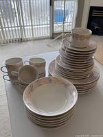 Stacked dinnerware set showing plates, bowls and cups with pastel floral rim pattern