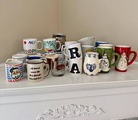 Group shot of all mugs, pint glass and travel mug on shelf