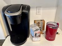 All items front view: Keurig brewer, boxed reusable filter, boxed water filter cartridges, red coffee grinder