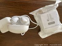 Loose white wireless earbuds in open charging case beside sealed bag containing second earbuds set, USB cable and manual